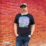 Man wearing a black t-shirt with a "Game On Pup" graphic design in front of a brick wall – Gamer Gay Pup Play T-Shirt – LGBTQ+ pride t-shirts US UK – Gay pride shirts collection – Made-to-order gay apparel