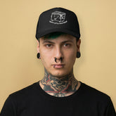 Tattooed Gay man wearing a Happy Little Cum Dump trucker cap with cartoon dumpster graphic on black mesh snapback hat - Backroom Gear
