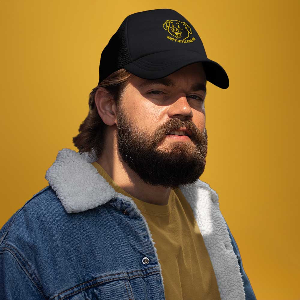 A gay bear wearing a black cap with a yellow pig graphic and the text 'Happy Little Piss Pig' on a yellow background - Black Happy Little Piss Pig trucker cap - watersports kink pride hat by BackRoomGear