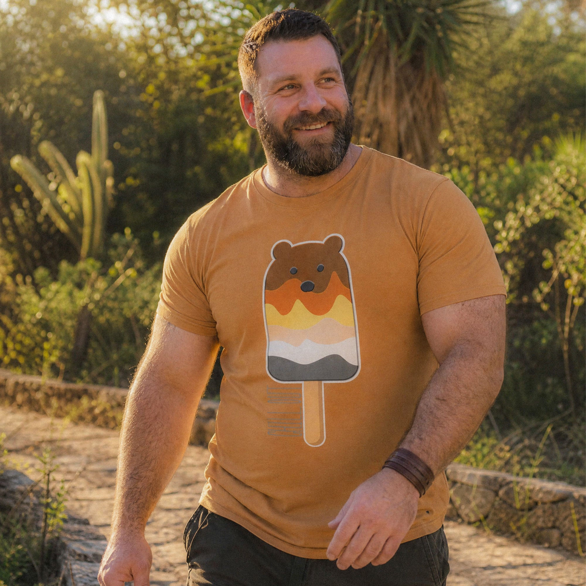 Man wearing a toast brown t-shirt with a bear popsicle design, standing outdoors - Bear Paddle Pop T-Shirt – Gay Bear Pride Flag Parody Tee – LGBTQ+ pride t-shirts US UK – Gay pride shirts collection – Made-to-order gay apparel