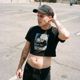 Gay Man wearing a Confess Crop Sniff Test, a black pup graphic crop top and a cap, standing on a street.