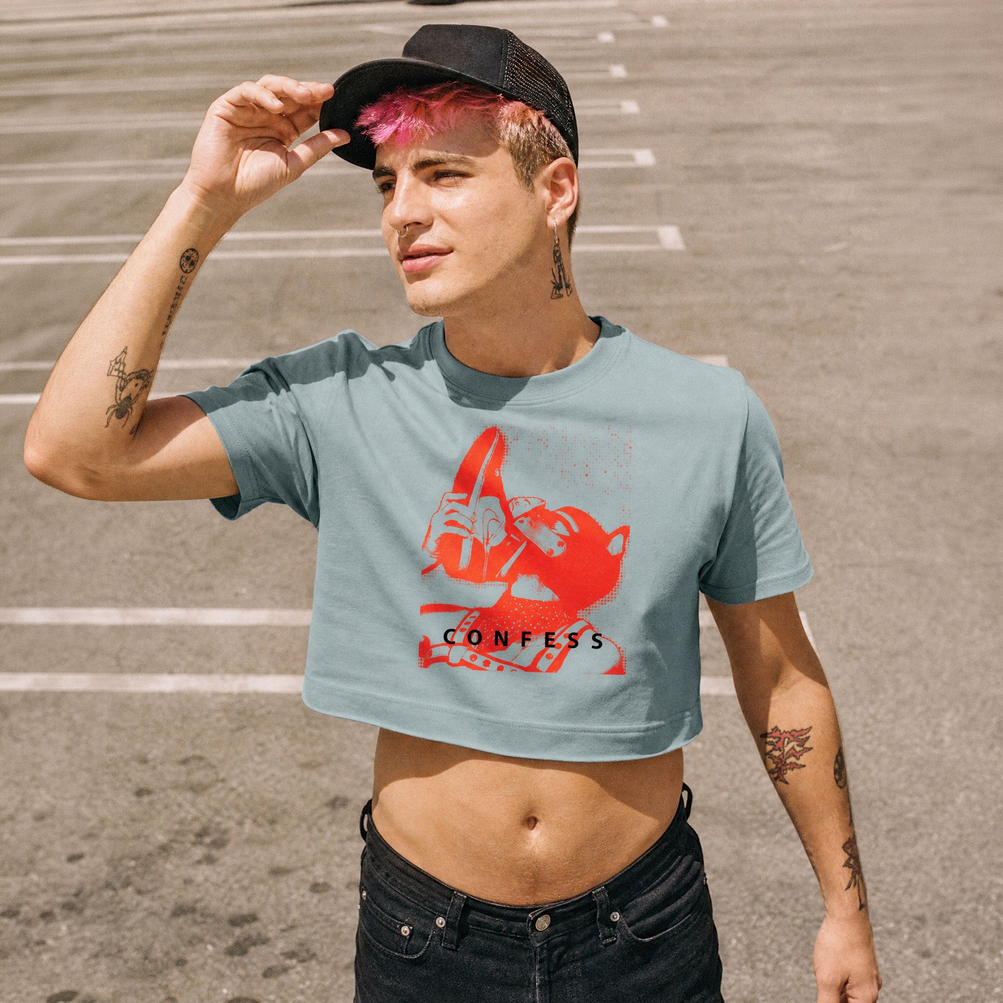 Man wearing a Confess Crop Sniff Test, mineral blue pup graphic crop top with a red sneaker pup graphic and text, standing outdoors.