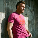 Lifestyle shot of a gay man wearing a berry pink t-shirt with a Sneaker Pup graphic design and 'CONFESS' text standing in front of a concrete wall