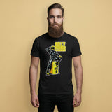 gay Man wearing a black t-shirt with a man in rubber with yellow helmet and shoes sitting on top of a square barrel of piss graphic design on a beige background - Black and yellow Sexy Rubber Flanders t-shirt - kinky latex rubber kink tee by BackRoomGear