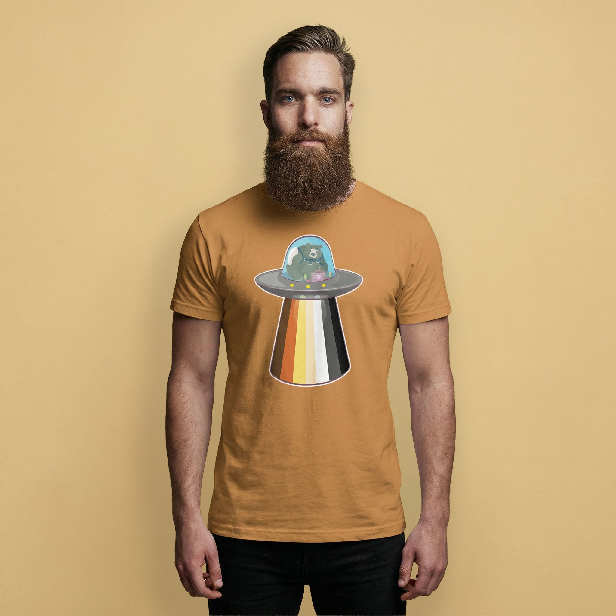 Gay Bear wearing a toast brown t-shirt with a Bear Pride flag UFO on a beige background - UFO Bear T-Shirt – Gay Leather Pride Tee for Bears – LGBTQ+ pride t-shirts US UK – Gay pride shirts collection – Made-to-order gay apparel