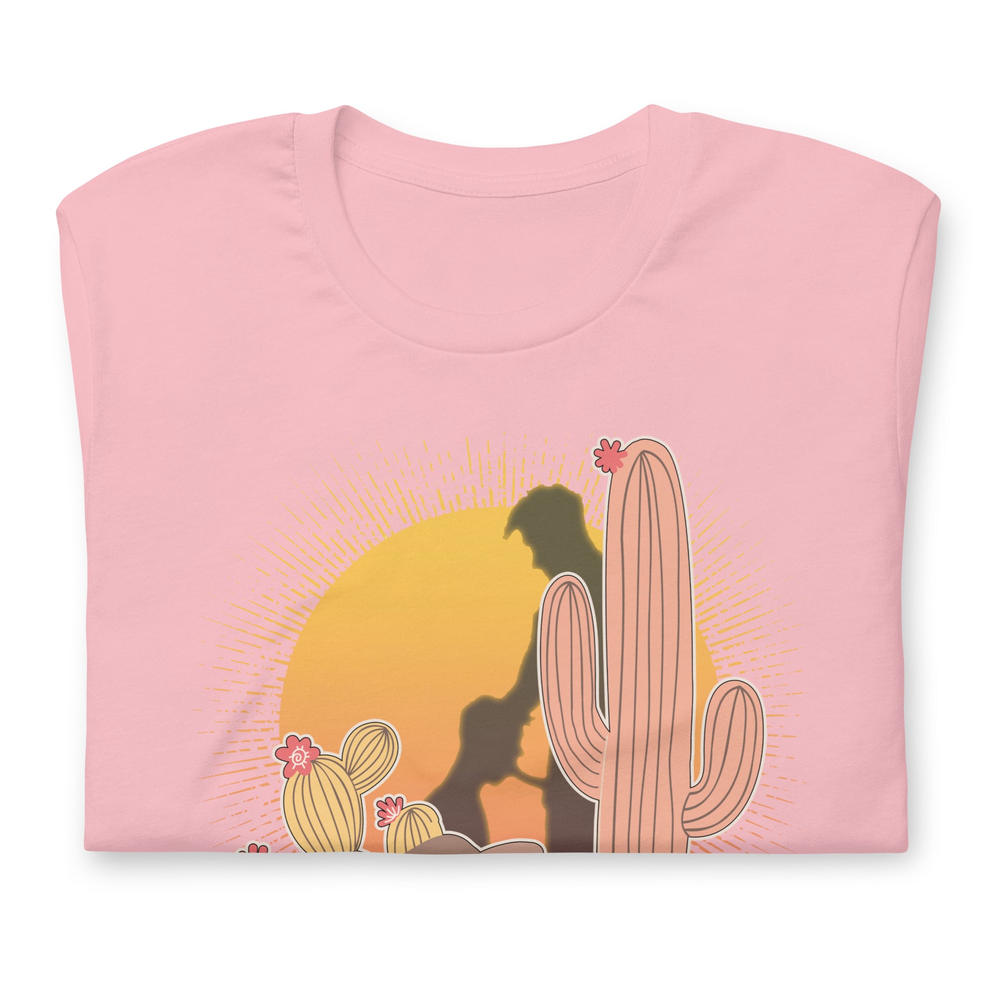 Folded pink shirt featuring a sunset with two silhouetted figures, one sitting sucking the one standing, surrounded by cacti - Vintage Brokeback Cowboy t-shirt - western gay pride tee by BackRoom Gear