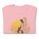 Folded pink shirt featuring a sunset with two silhouetted figures, one sitting sucking the one standing, surrounded by cacti - Vintage Brokeback Cowboy t-shirt - western gay pride tee by BackRoom Gear