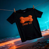 Black t-shirt with orange bone graphic and 'CHEW TOY' text on a clothesline over a beach at night.