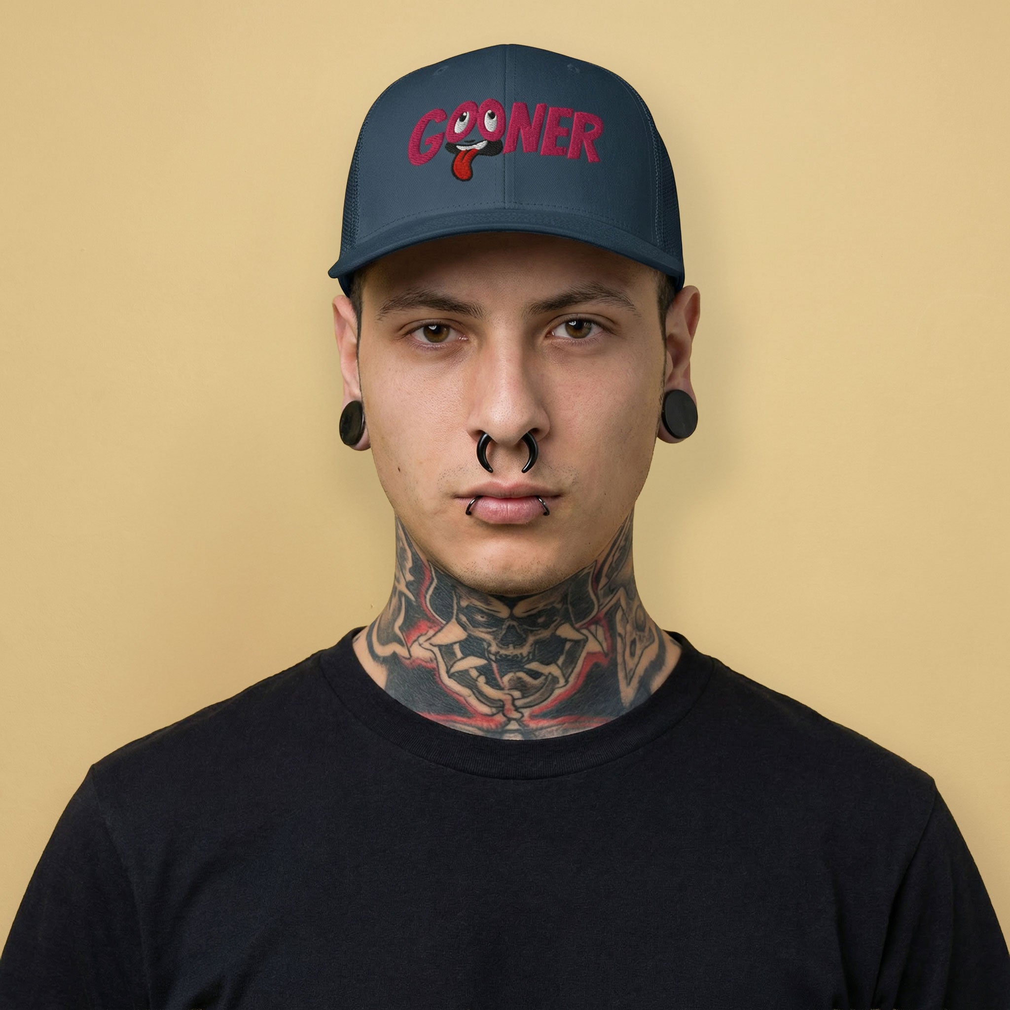 Man wearing a navy cap with 'GOONER' text, rolled eyes and hanging tongue on a beige background - Backroom Gear