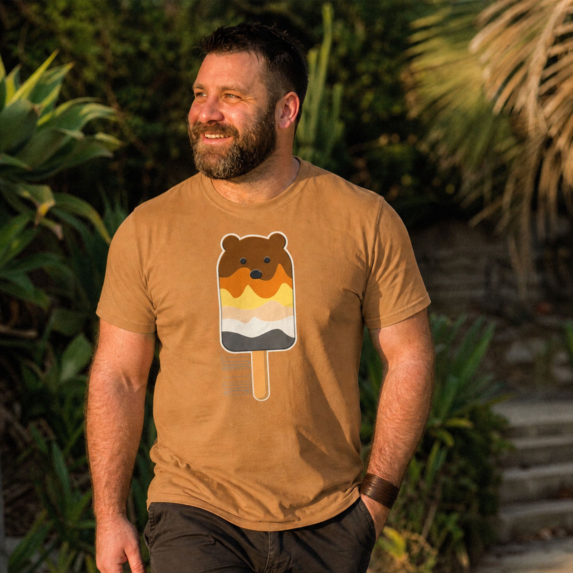 Man wearing a toast brown t-shirt with a bear popsicle design, standing outdoors - Bear Paddle Pop T-Shirt – Gay Bear Pride Flag Parody Tee – LGBTQ+ pride t-shirts US UK – Gay pride shirts collection – Made-to-order gay apparel