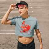 Man wearing a Confess Crop Sniff Test, mineral blue pup graphic crop top with a red sneaker pup graphic and text, standing outdoors.