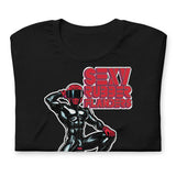 Folded black t-shirt with a man in rubber with red helmet and shoes sitting on top of a square barrel of Lube graphic design on a beige background  - Black and red Sexy Rubber Flanders t-shirt - kinky latex rubber kink tee by BackRoomGear