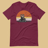 Maroon t-shirt with a bear on a motorcycle graphic against a beige background - Leather Biker Bear T-Shirt - Cute Retro Sunset Design – Gay pride shirts collection – LGBTQ+ pride t-shirts US UK – Made-to-order gay apparel